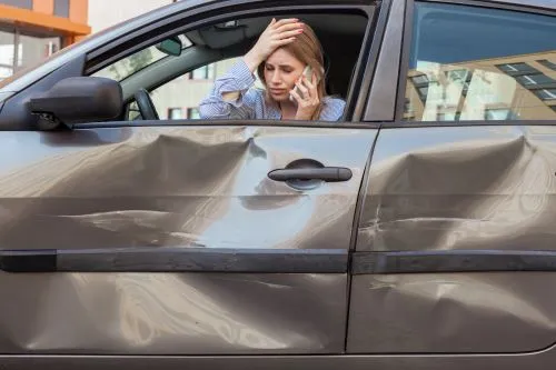 A woman sits in her car and calls the police after a car accident.