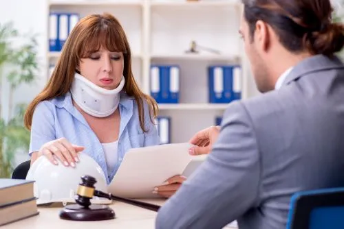 An injured woman wearing a neckbrace reviews paperwork with a lawyer after a car accident. 