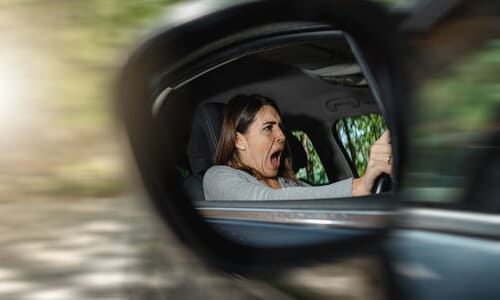 A terrified female driver as seen through her side view mirror as an accident is about to occur.