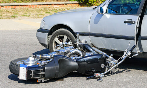 A motorcycle lying on its side after having collided with a grey automobile.