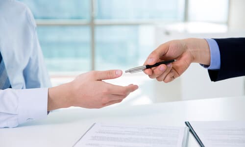 A personal injury lawyer handing a client a pen to sign a settlement agreement.